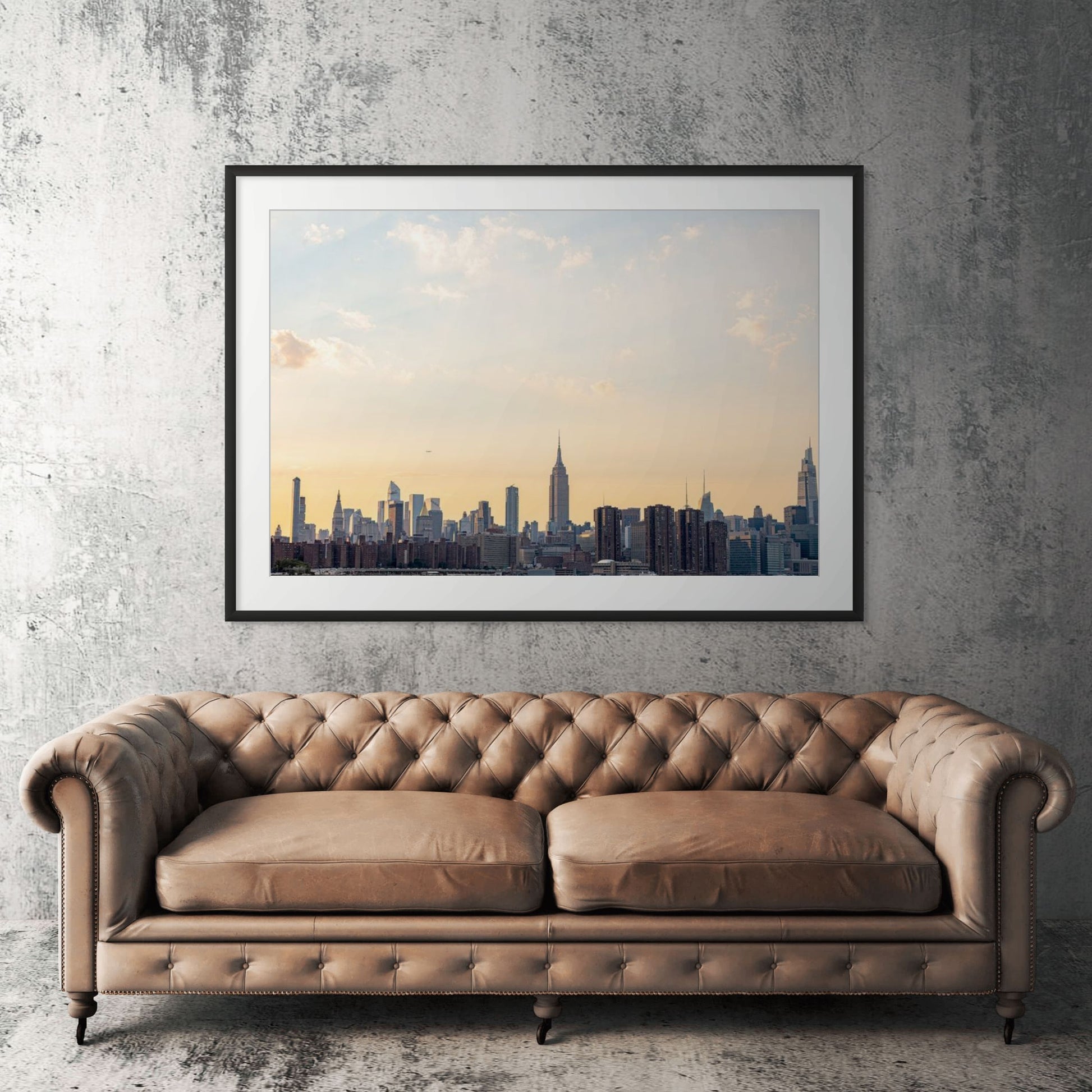 Manhattan skyline framed print displayed above tan leather sofa in living room