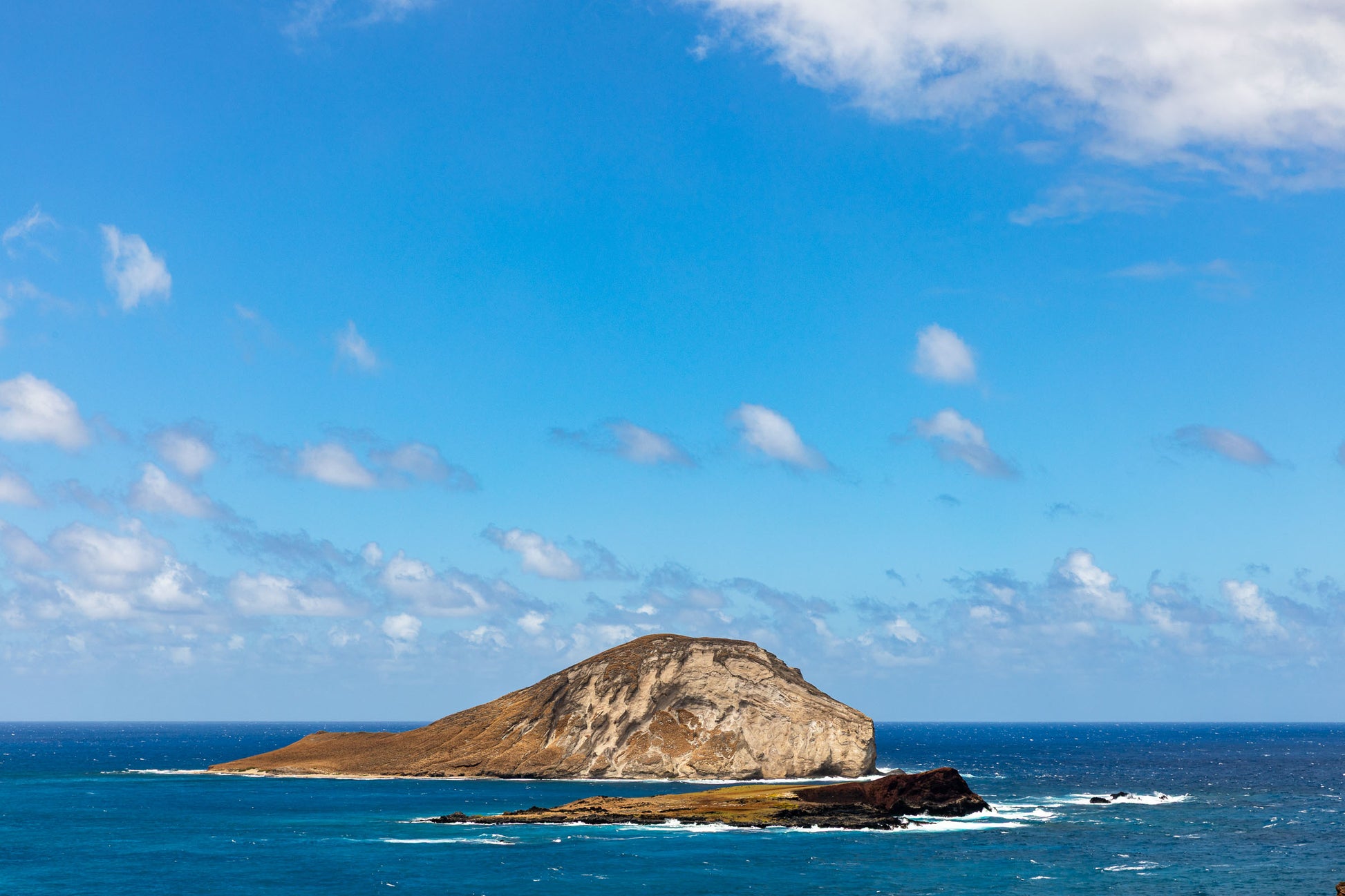 Small island off Oahu coast with turquoise Pacific Ocean water and waves Hawaii