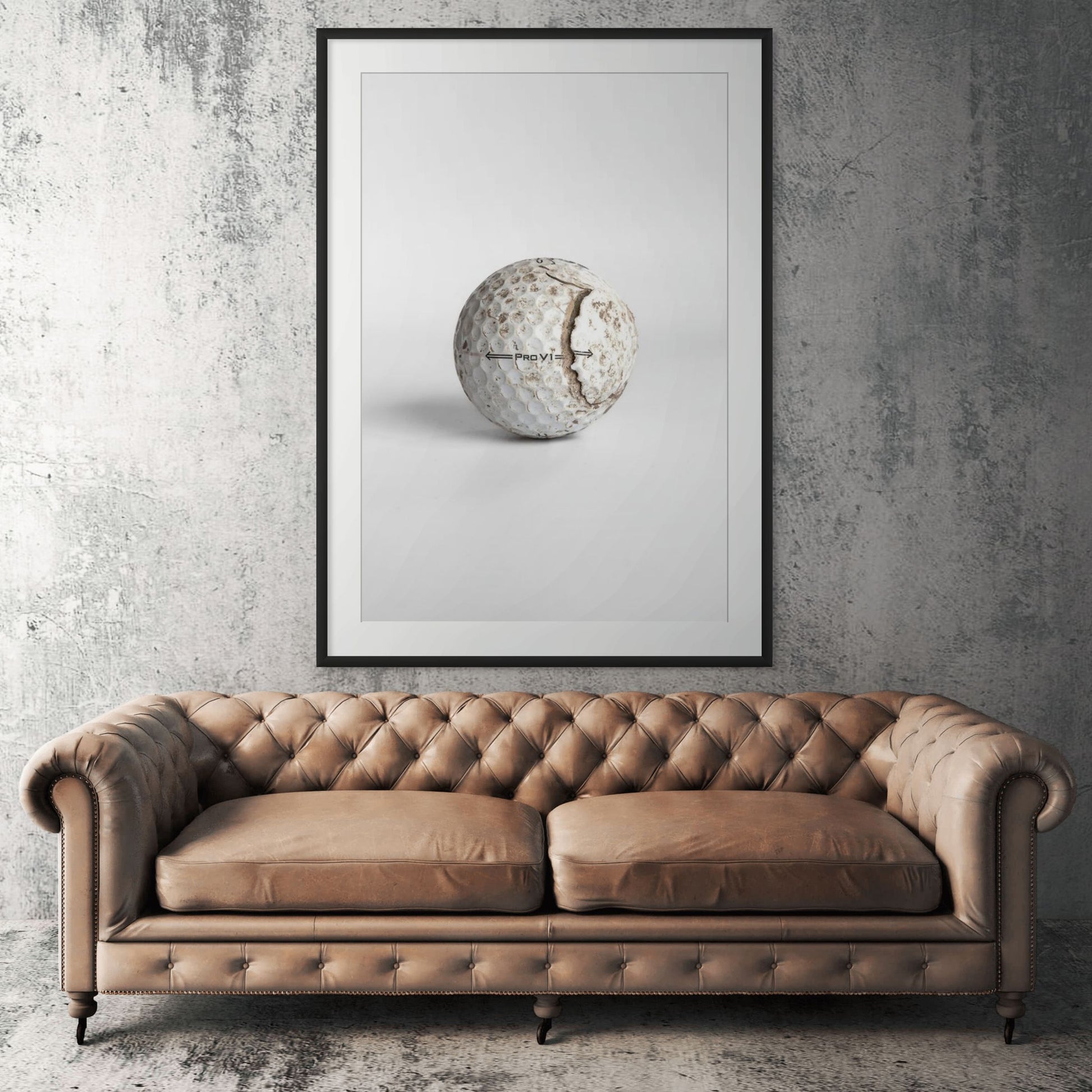 Titleist Pro V1 aged cracked golf ball framed print displayed above tan leather sofa in living room