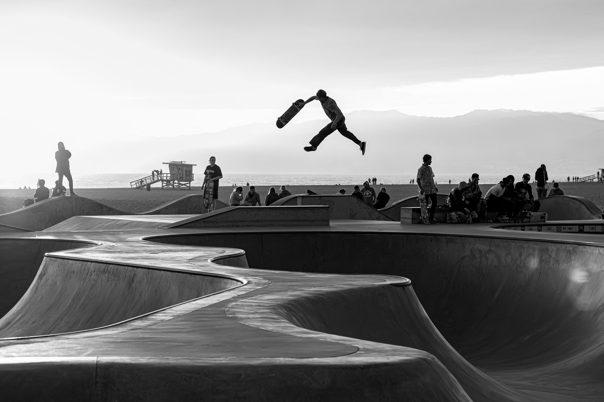 Skateboarder mid-air silhouette at Venice Beach skatepark with mountains and ocean California